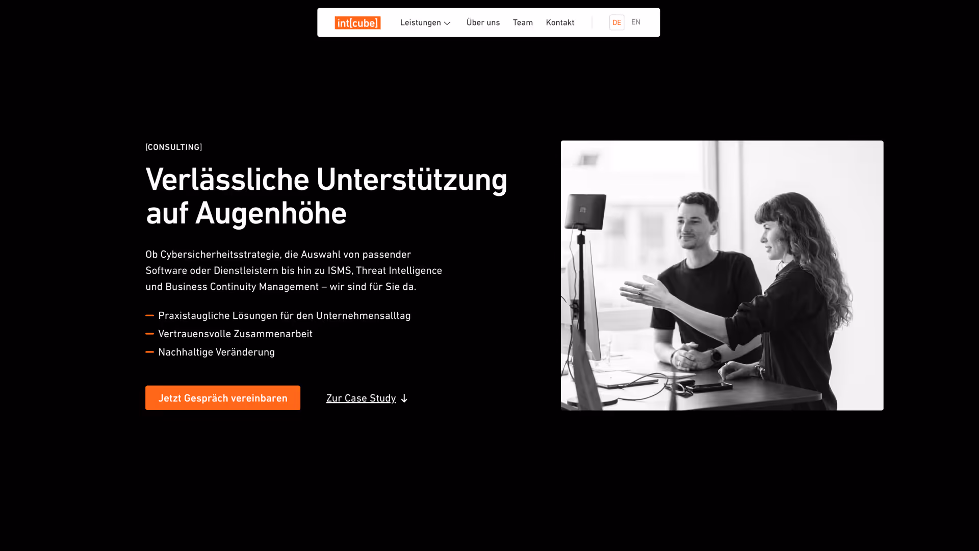 Schwarzweiß Foto eines Mannes und einer Frau, die sich vor einem Computermonitor in einem hellen Büro austauschen.