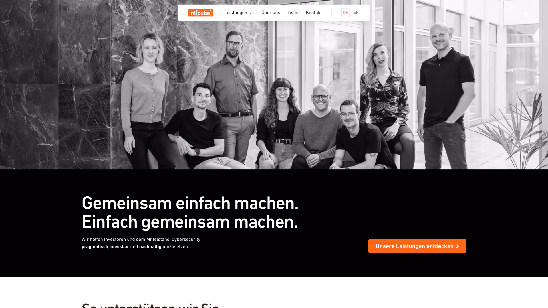 Gruppenporträt von acht lächelnden Personen, vier sitzend und vier stehend, in einem modernen Büro mit großen Fenstern und Marmorwänden.