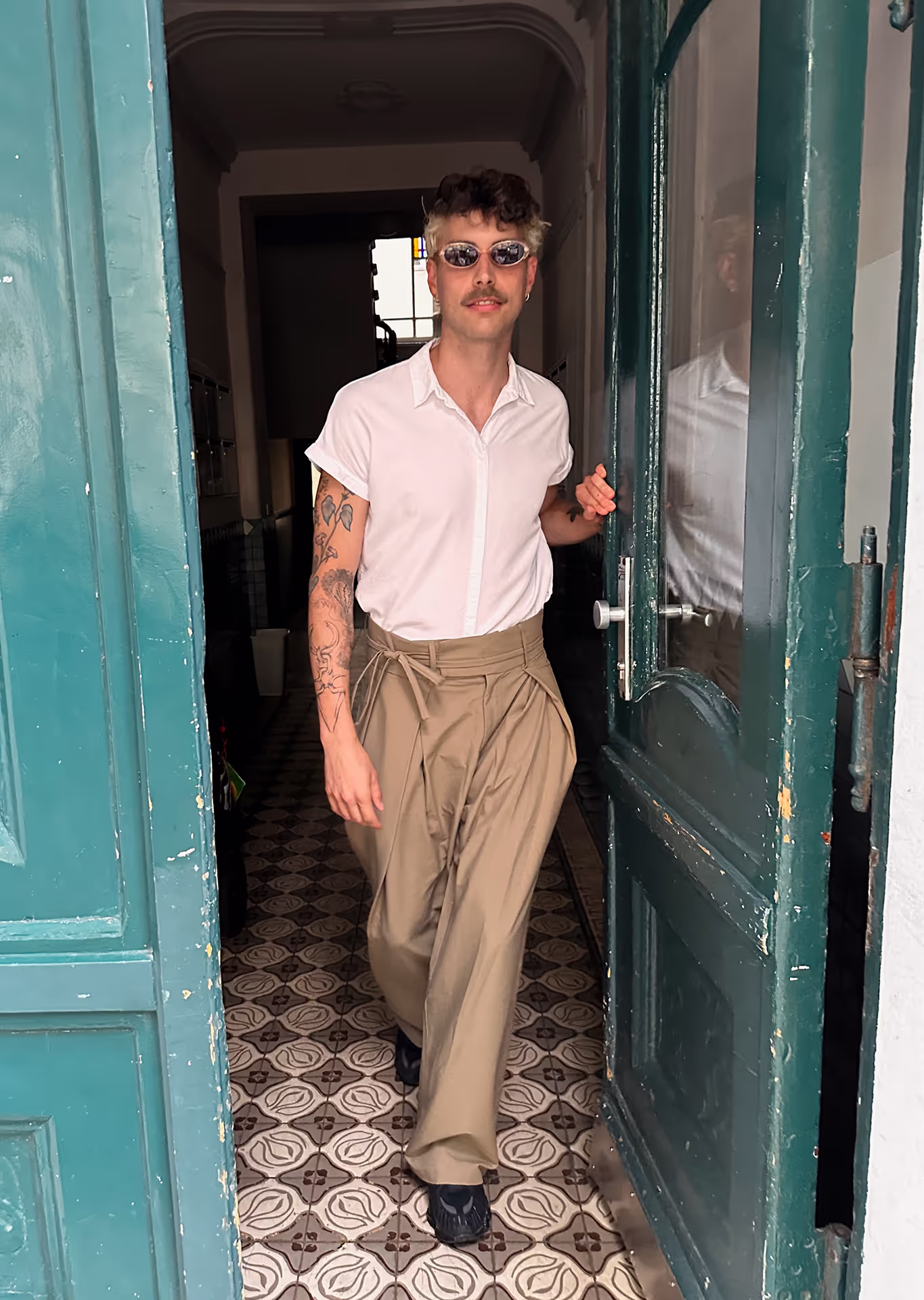 Thomas Etscheidt in weißem Hemd, weiter beiger Hose und Sonnenbrille, geht durch einen Türrahmen.